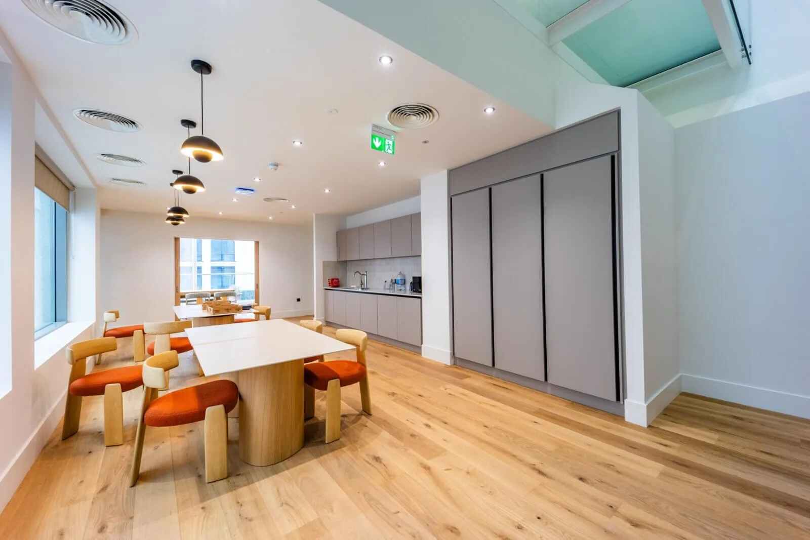 Window-side collaboration room with pale oak tables, rust-coloured chairs and a compact kitchen