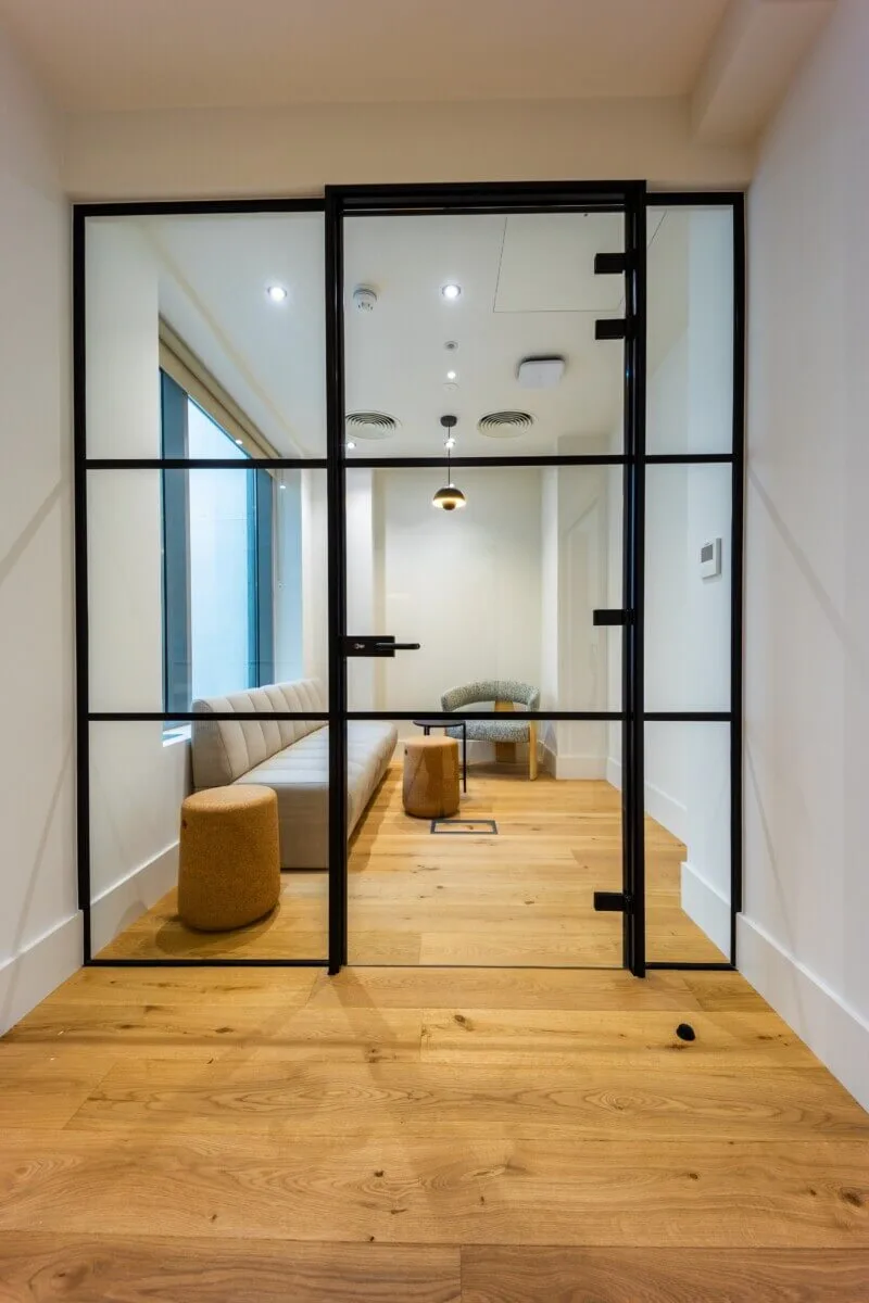 Compact enclosed retreat with black-framed glazing, a sofa and timber floor