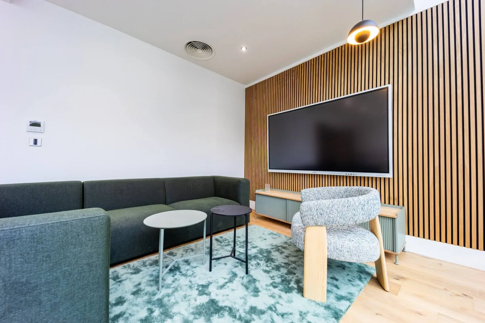 Quiet lounge with a deep green sofa, patterned armchair and oak slatted media wall